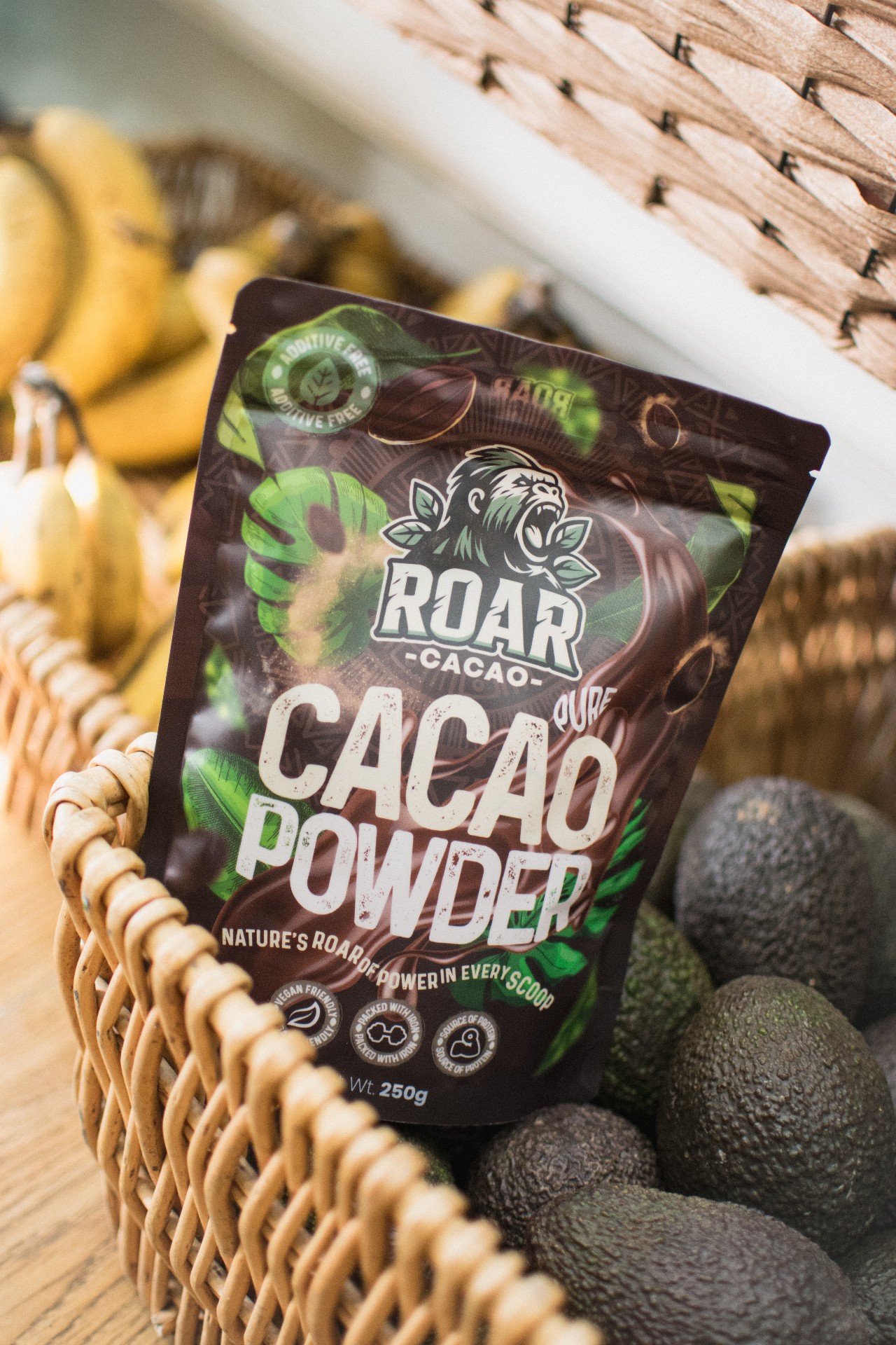 Roar Cacao pouch nestled in a wicker basket with bananas and avocados