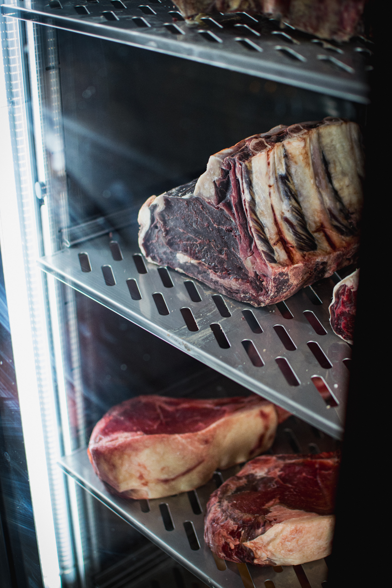 Dry-aged steaks displayed on stainless steel shelves in a butcher's fridge