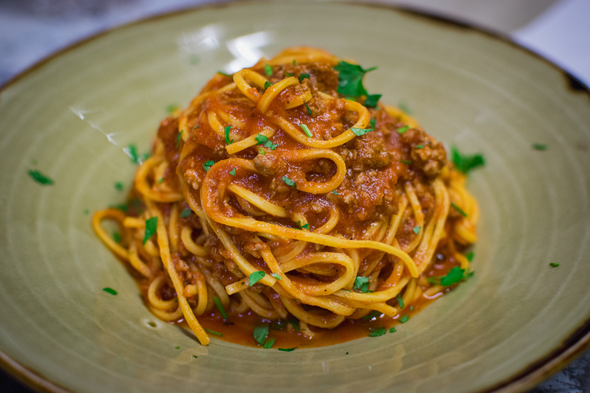 Spaghetti bolognese with parsley on a green ceramic plate