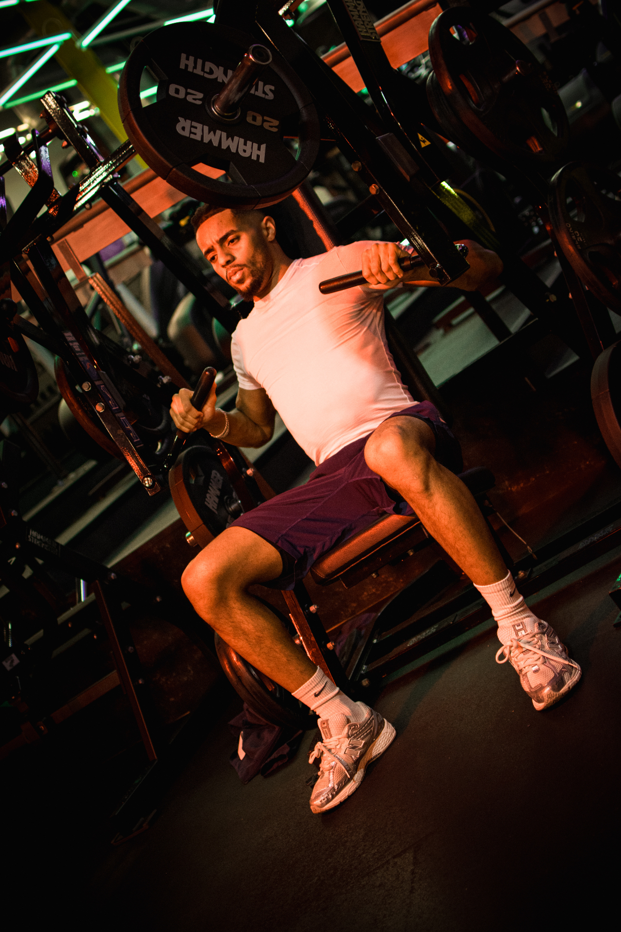 Athlete pressing on a plate-loaded shoulder machine in moody neon light
