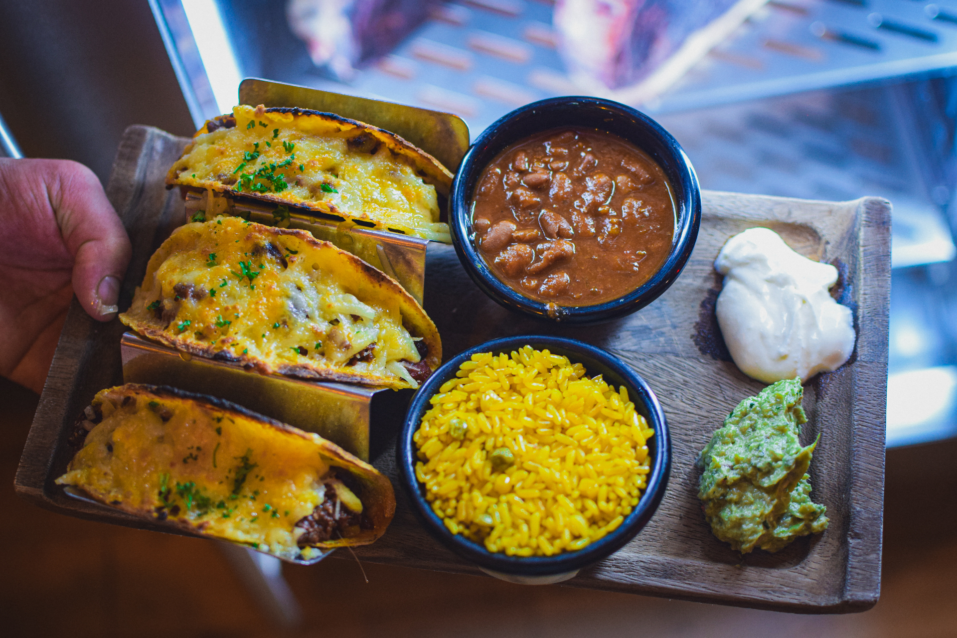 Cheesy beef tacos served with rice, beans, guacamole and sour cream on a wooden board